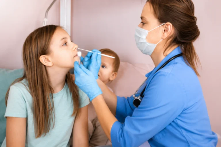 Blog 1 A female doctor wearing a face mask and gloves using a nasal swab to examine a young girl during a clinical consultation.