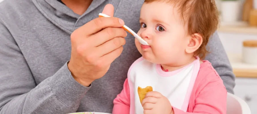 how long does oral immunotherapy take- Parent feeding a baby with a spoon, illustrating parental support and feeding routines during childhood food allergy care.
