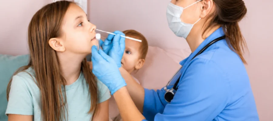 A female doctor wearing a face mask and gloves using a nasal swab to examine a young girl during a clinical consultation.